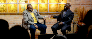 Mark Anthony Neal and Bakari Kitwana, both African American men in their fifties each wearing a suit seated and laughing in front of an audience