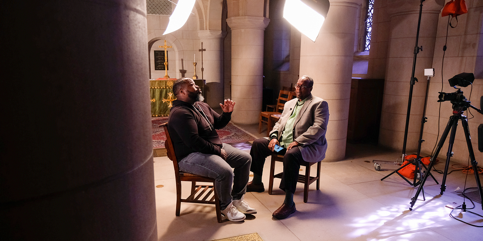 two men sit in a make-shift studio speaking to each other